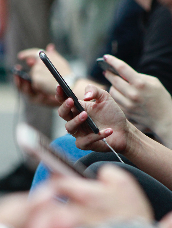 A side-on view of some people sat on a bench using their mobile phones